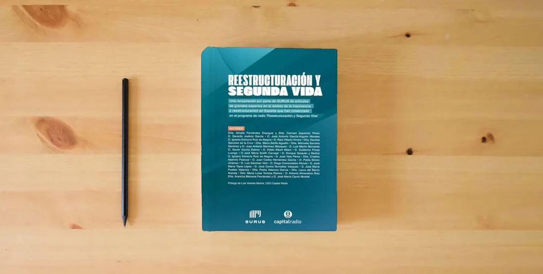 The book Reestructuración y Segunda Vida: Una recopilación por parte de SURUS de artículos de grandes expertos en el ámbito de la insolvencia y reestructuración en España que han colaborado en Capital Radio} is on the table